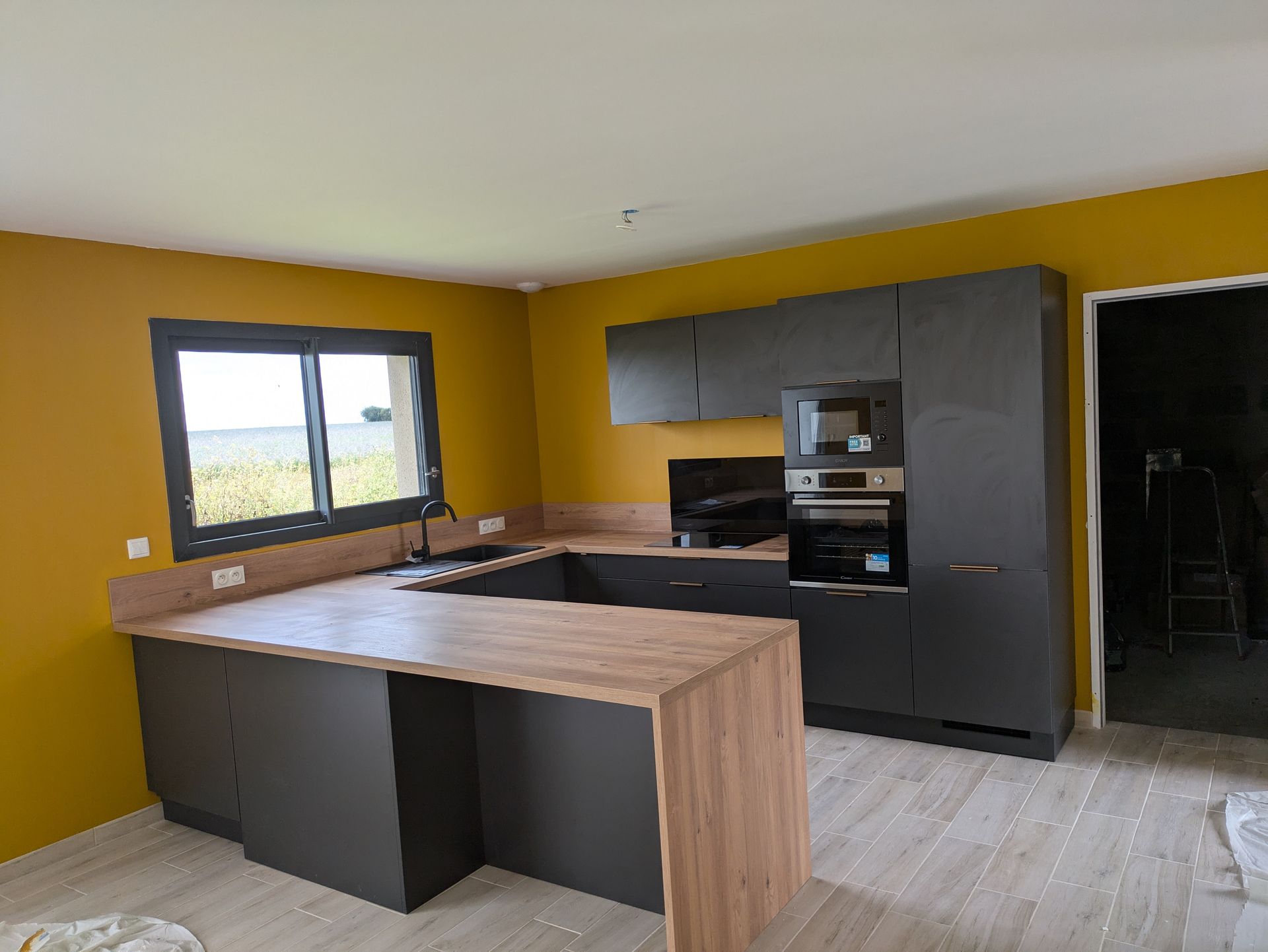 Cuisine moderne avec placards gris foncé, comptoirs en bois et murs jaune moutarde.