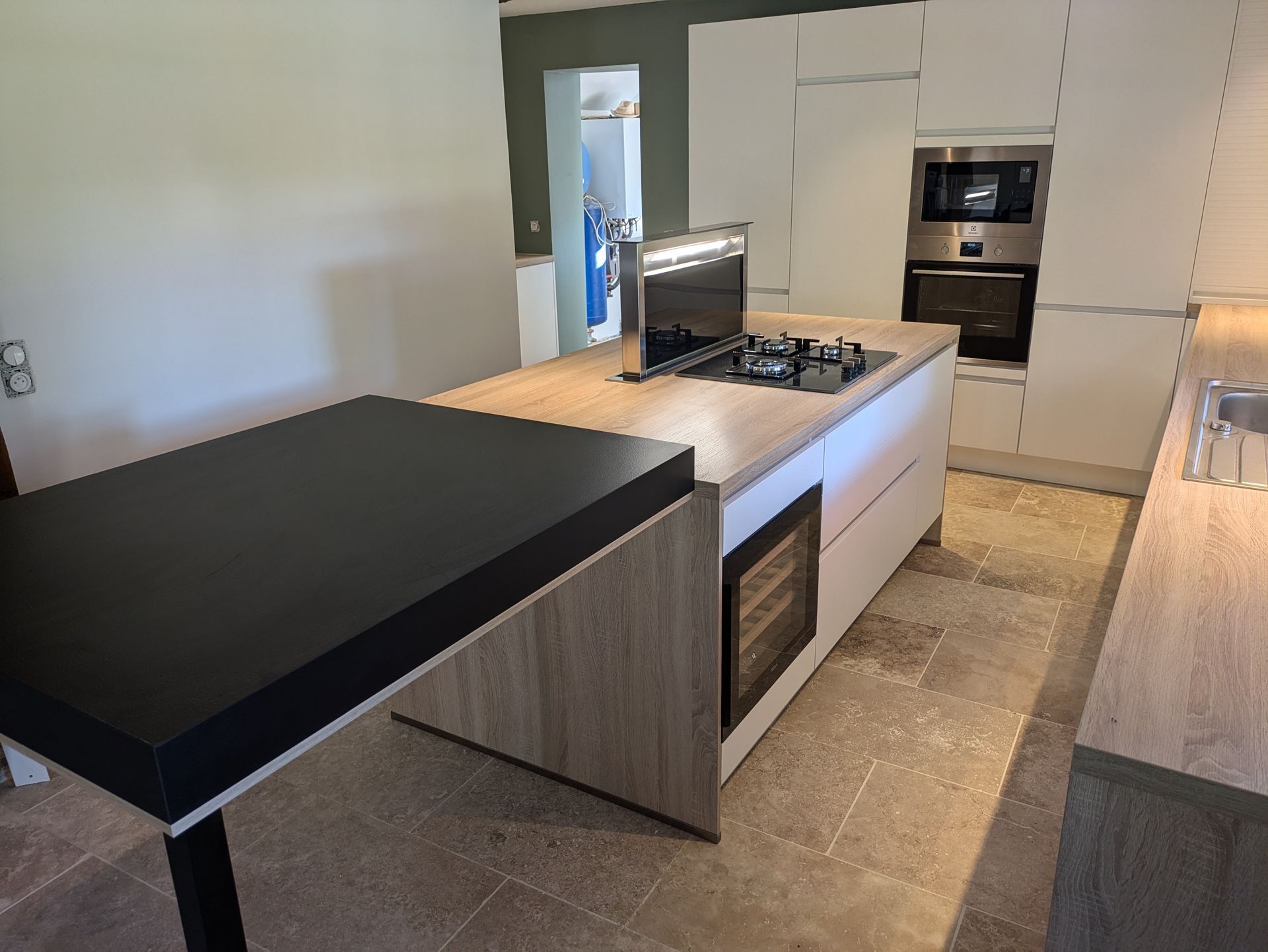 Cuisine moderne avec îlot central, plaque de cuisson, cave à vin et extension de plan de travail noire.