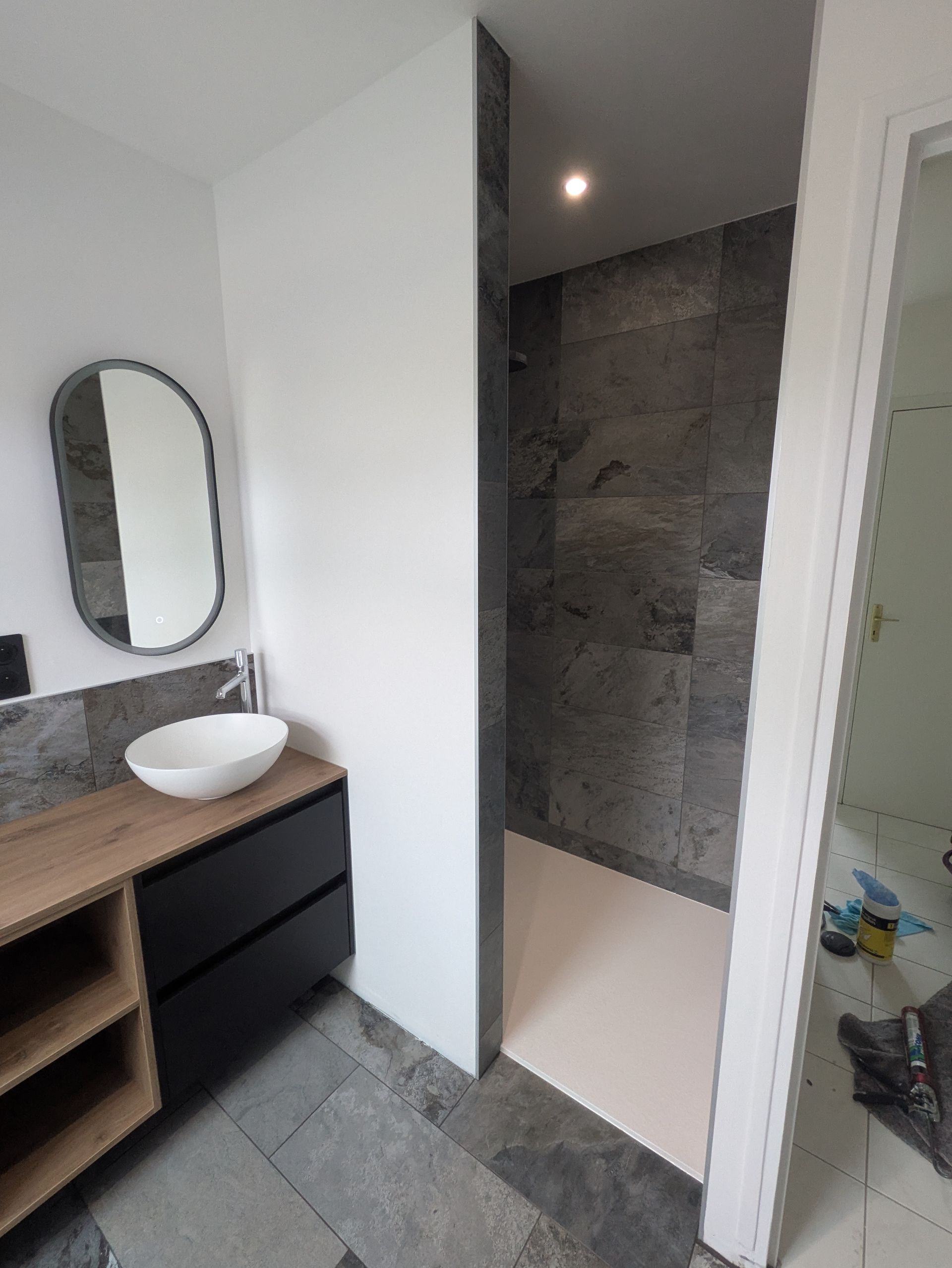 Salle de bains moderne avec douche, meuble-lavabo et grand miroir. Dominante de gris et de blanc.
