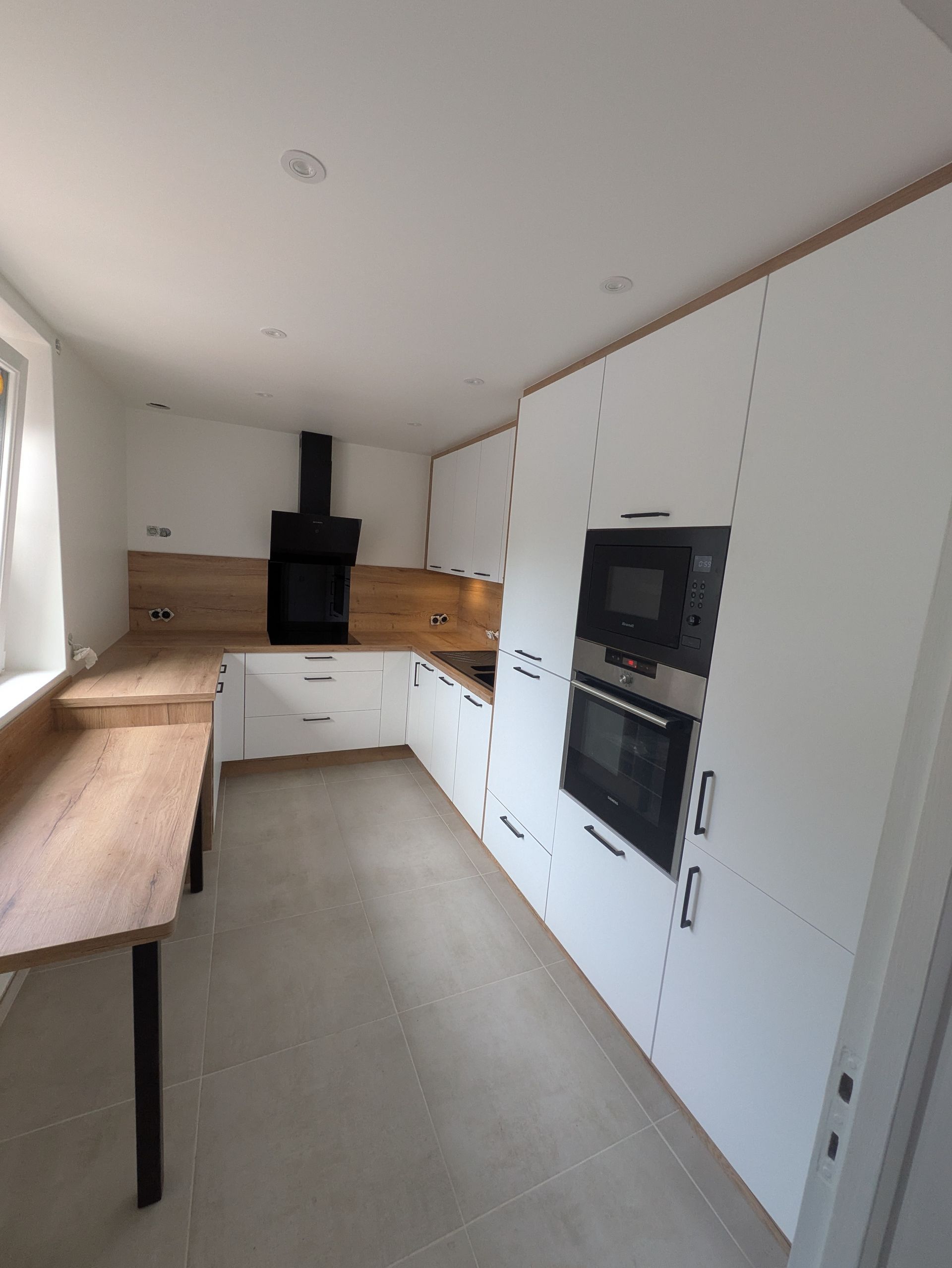 Cuisine blanche avec des éléments en bois, notamment les comptoirs et une hotte aspirante noire.