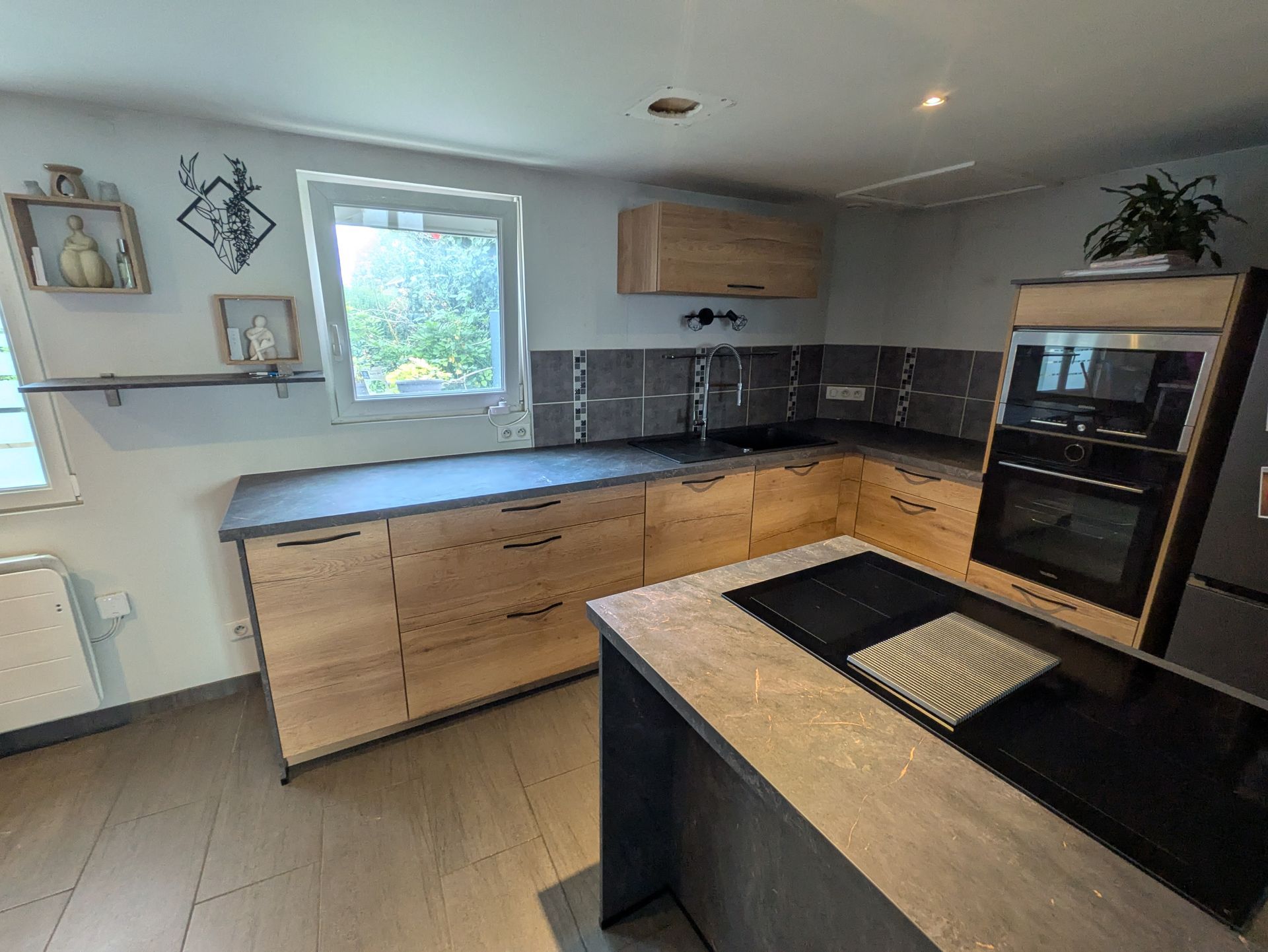 Cuisine moderne avec placards en bois clair, plans de travail foncés et îlot central avec plaque de cuisson noire.