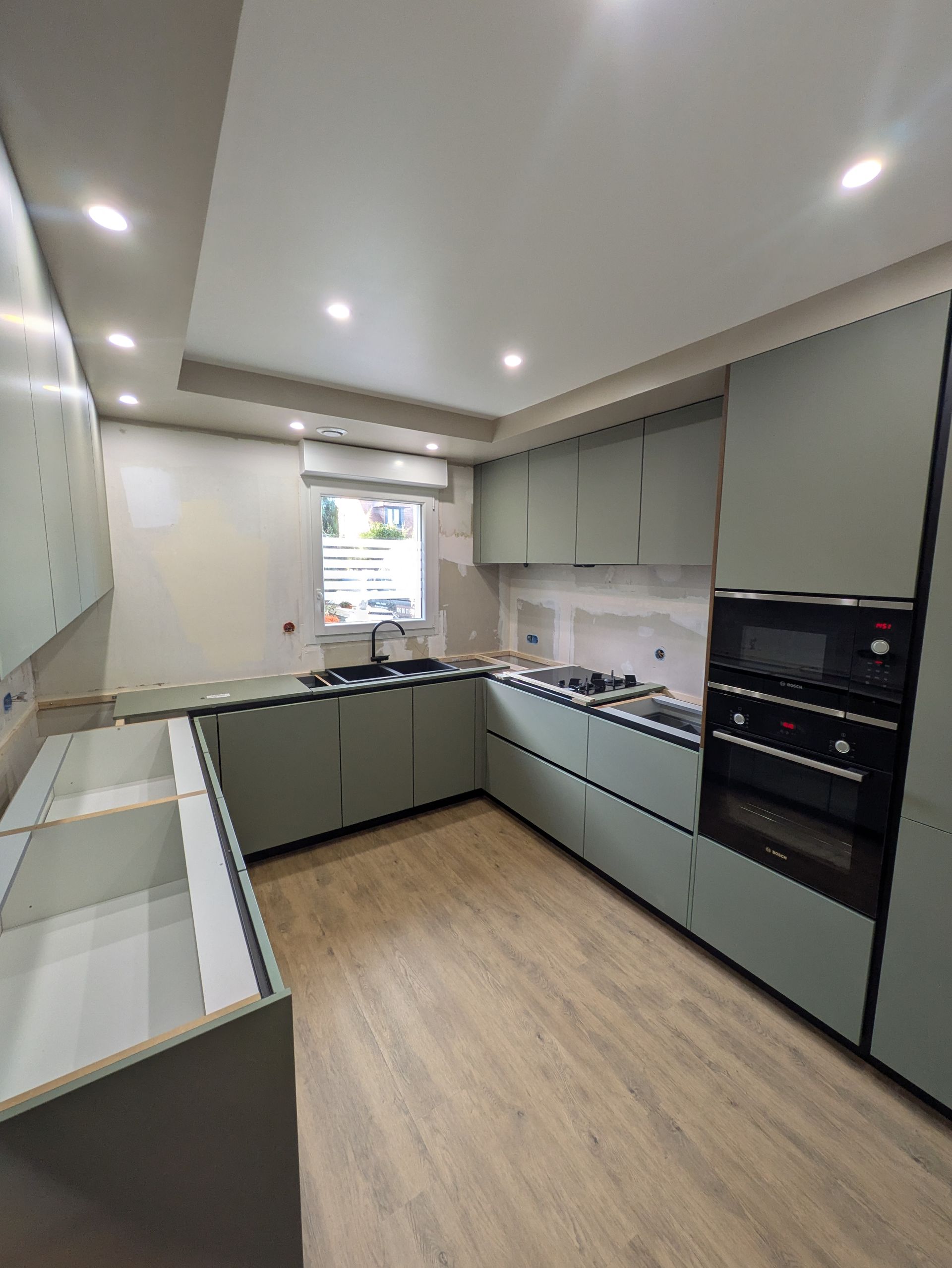 Cuisine moderne récemment rénovée avec des armoires vert sauge, un parquet clair et un éclairage encastré.