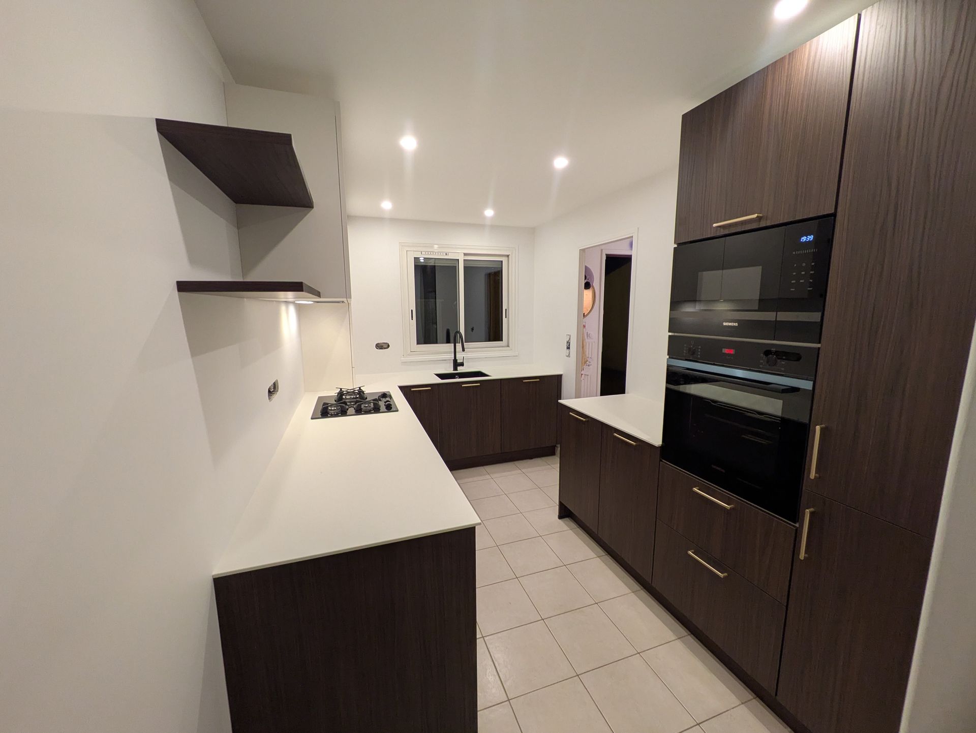 Cuisine moderne avec placards brun foncé, plans de travail blancs et four encastré.