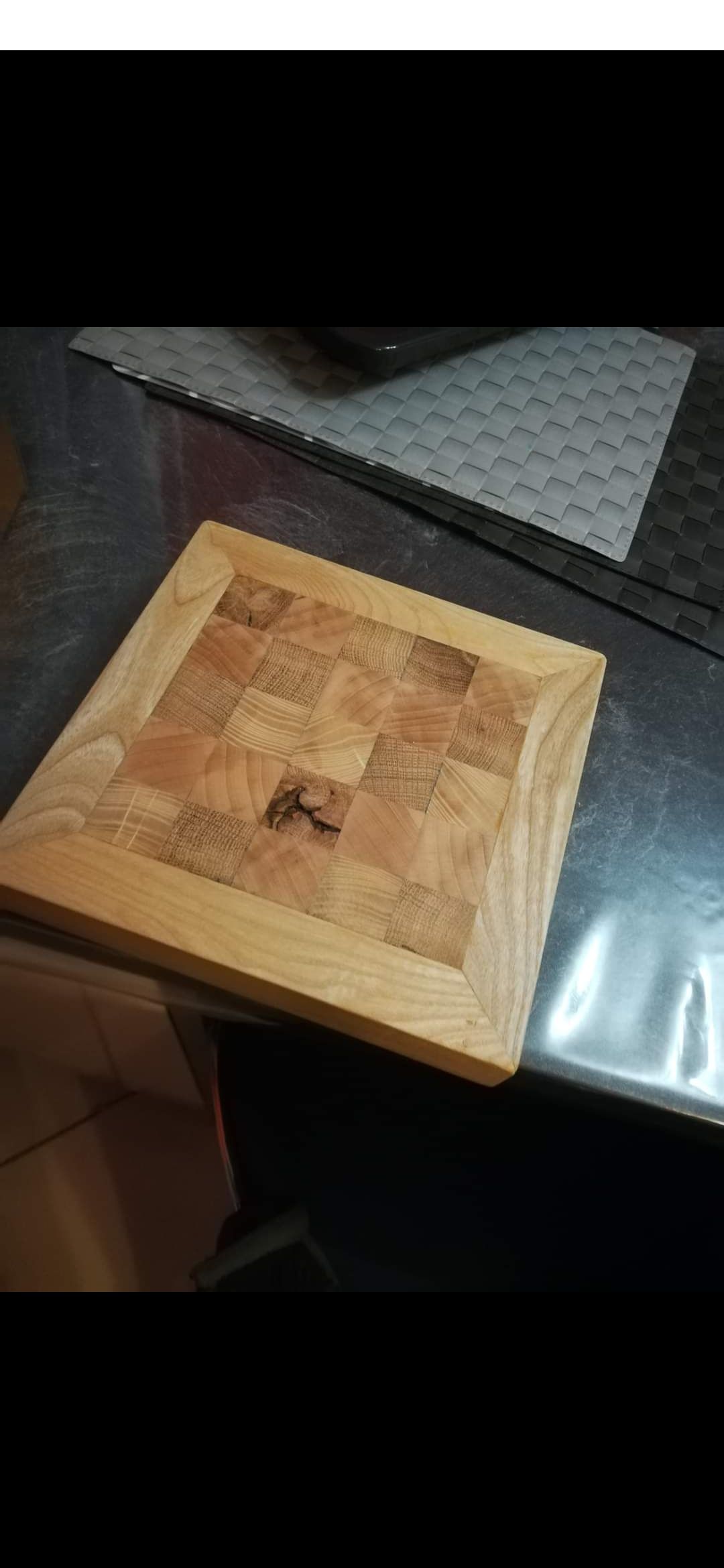 Un bloc carré en bois avec un motif à damier sur une surface métallique.