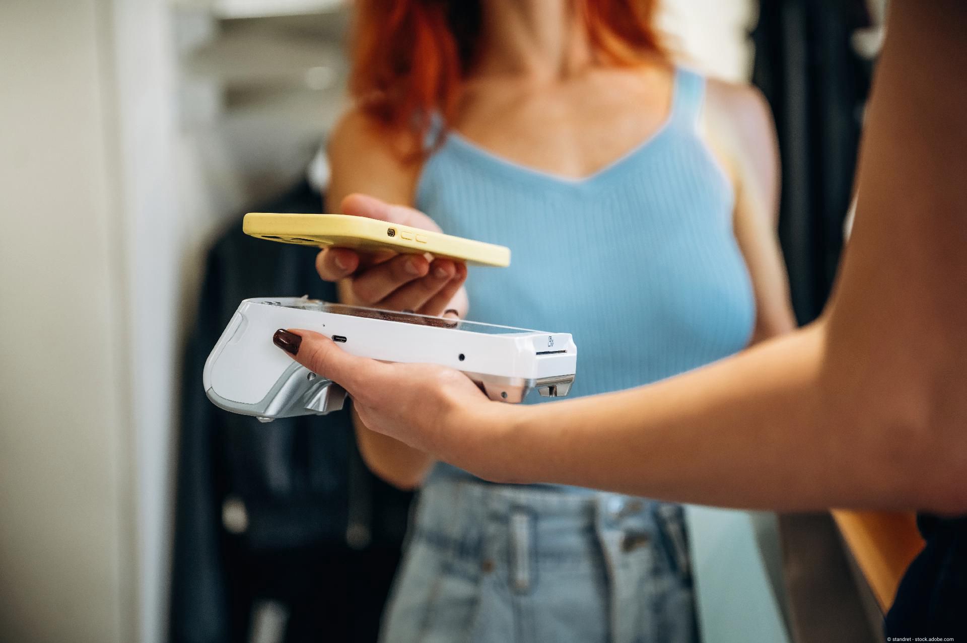 Eine junge Frau beim kontaktlosen bezahlen mit ihrem Handy