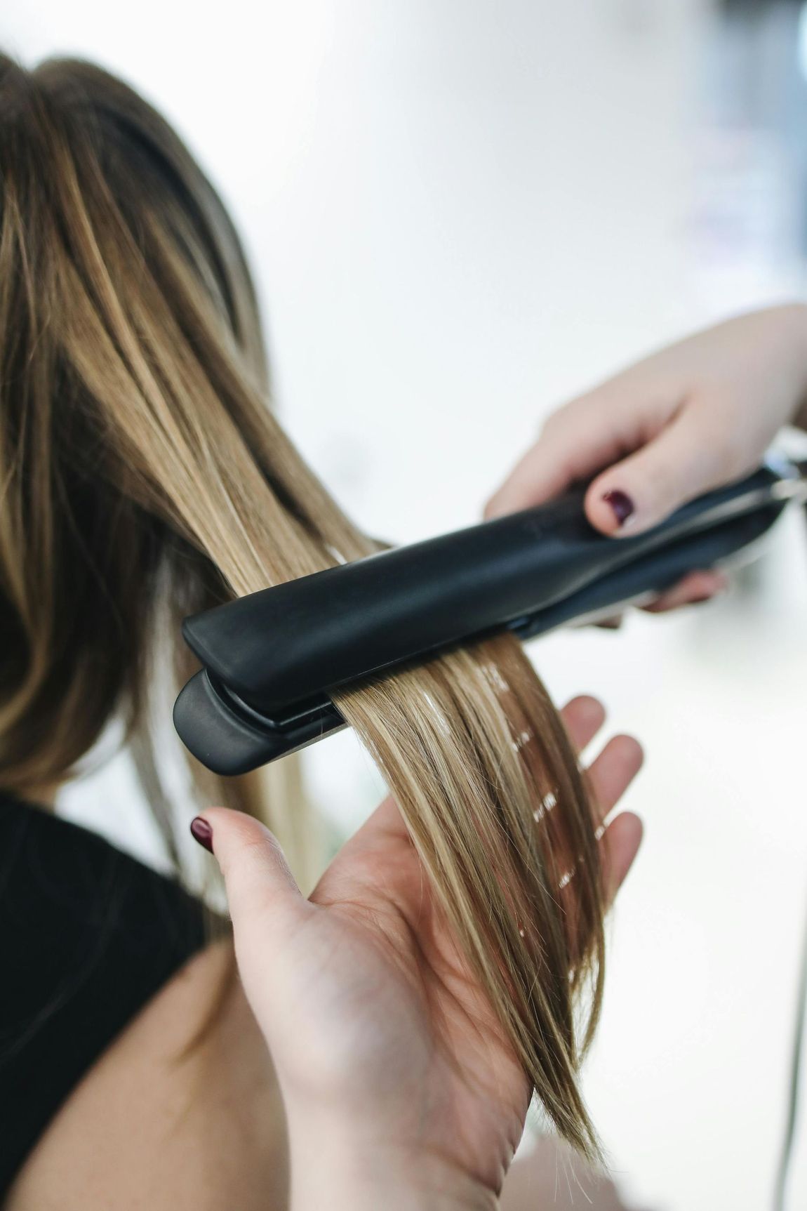 Peluquera alisando cabello rubio con una plancha negra en un salón de belleza.