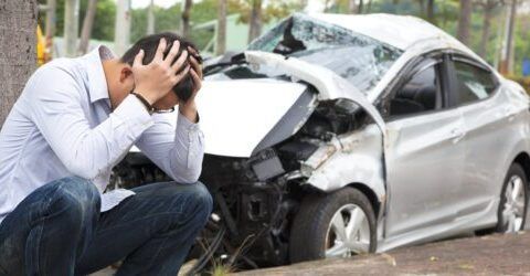 Un hombre está arrodillado delante de un coche averiado.