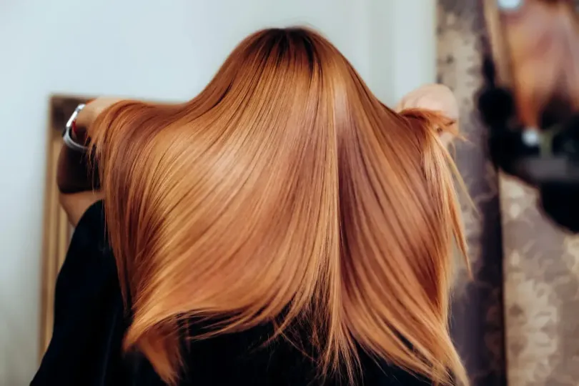 Mujer sosteniendo un cabello castaño rojizo, largo y liso en un salón.