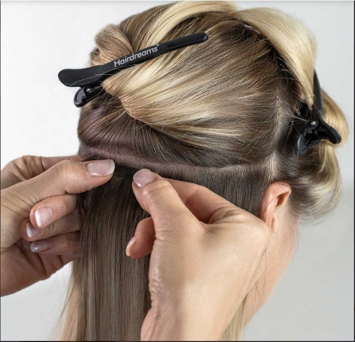 Manos colocando extensiones de cabello en cabello rubio.