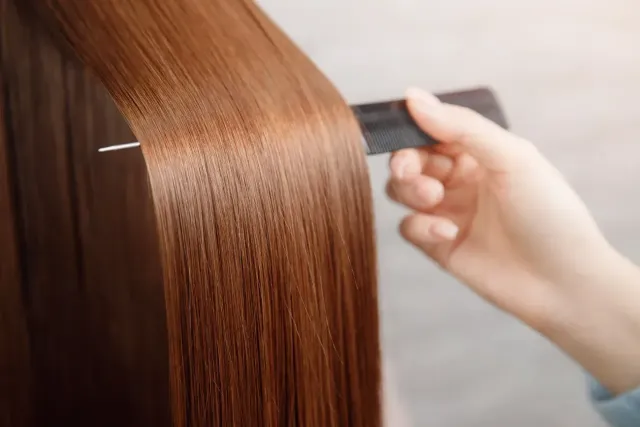 Peinando a mano cabello castaño, liso y brillante con un peine negro.