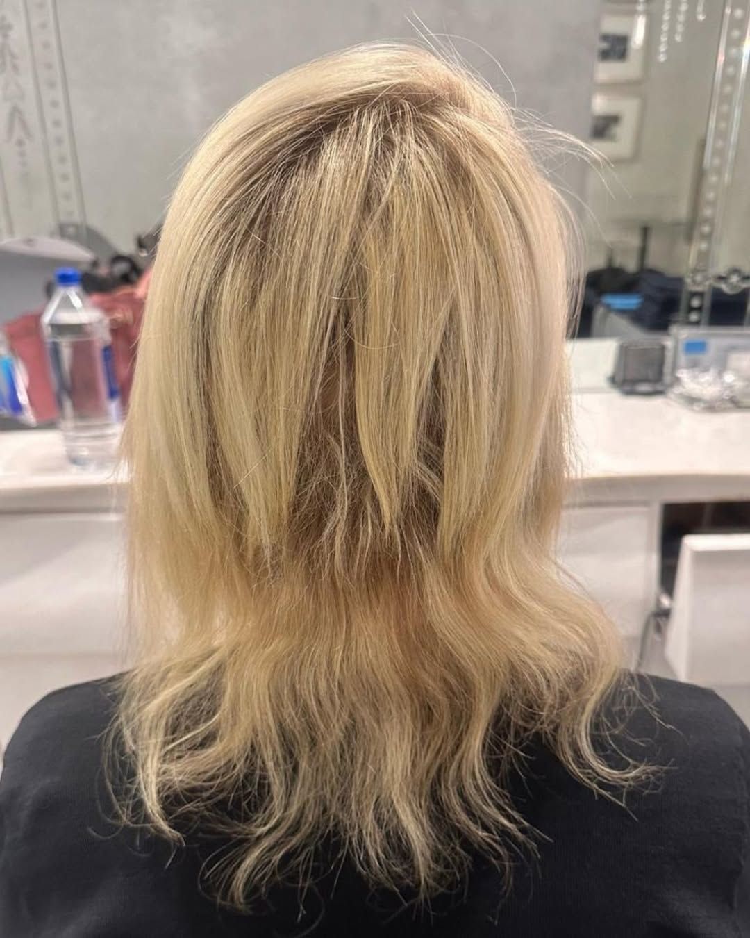 Cabello rubio, corte a media melena, vista de espaldas. Sentada en un salón de belleza.