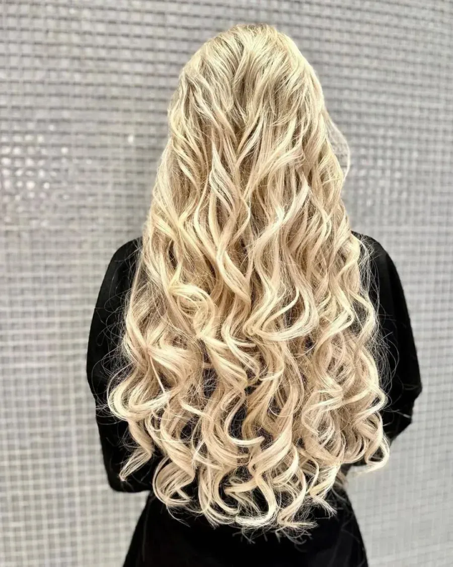 Cabello rubio largo y ondulado que cae en cascada por la espalda de una persona que viste una camiseta negra.