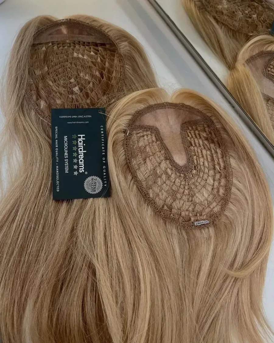 Dos postizos rubios con red y etiqueta de producto sobre superficie blanca.