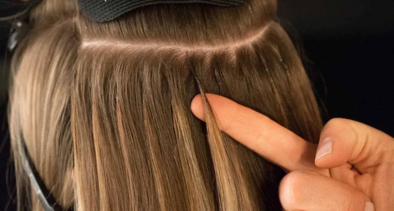 Manos colocando extensiones de cabello en cabello castaño con una herramienta; primer plano.