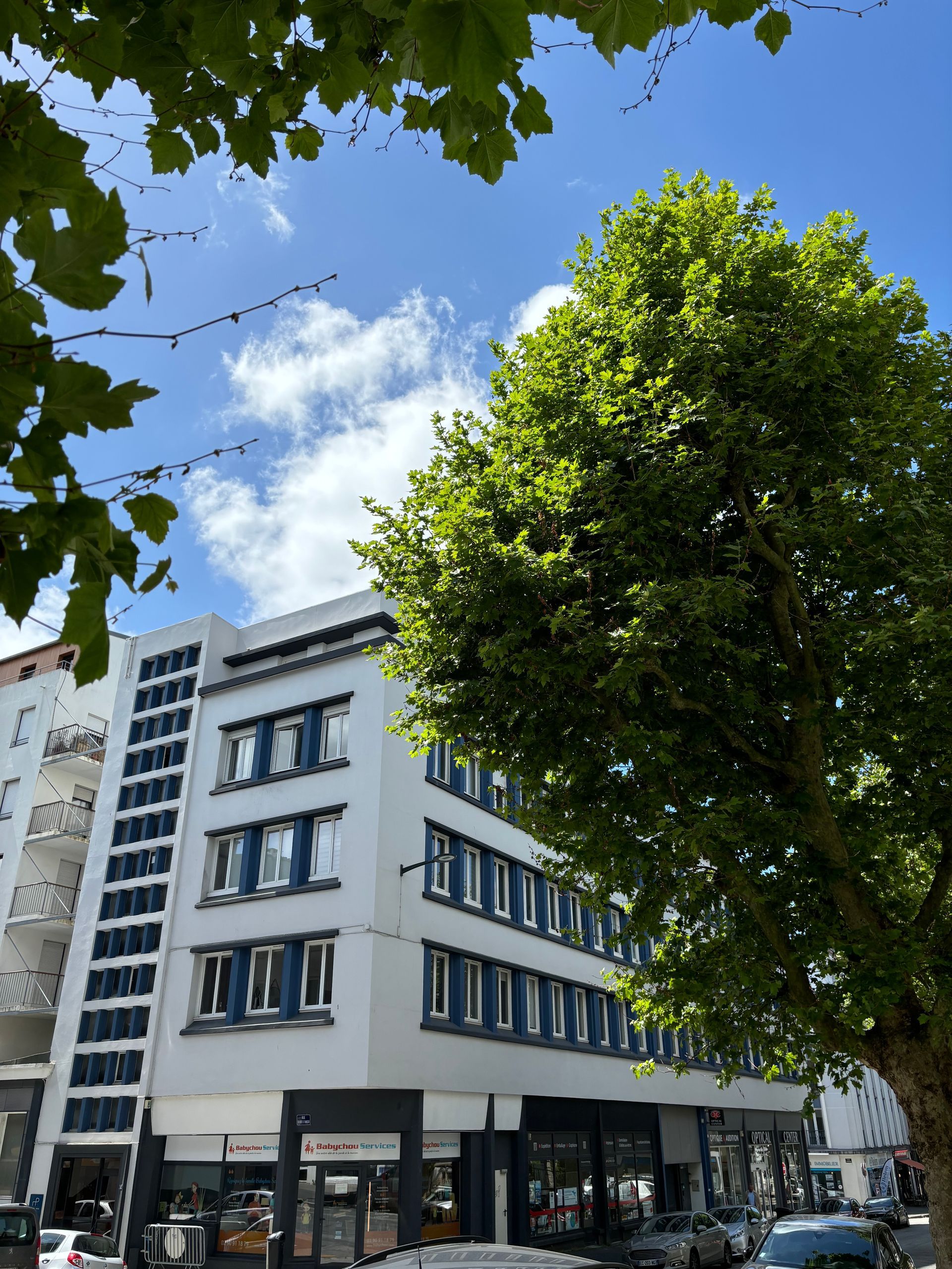 Un immeuble blanc à plusieurs étages, aux fenêtres encadrées de bleu.