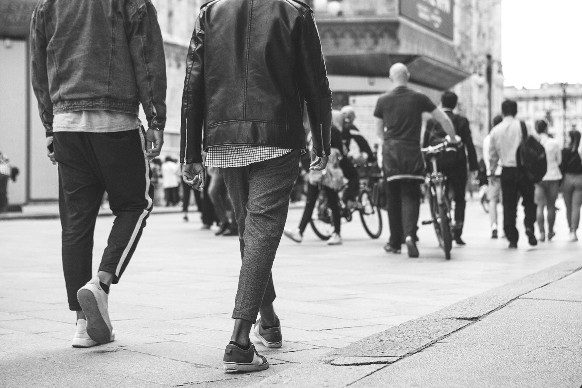 Une photo en noir et blanc, prise en contre-plongée, de personnes marchant dans une rue de la ville, vues de dos.