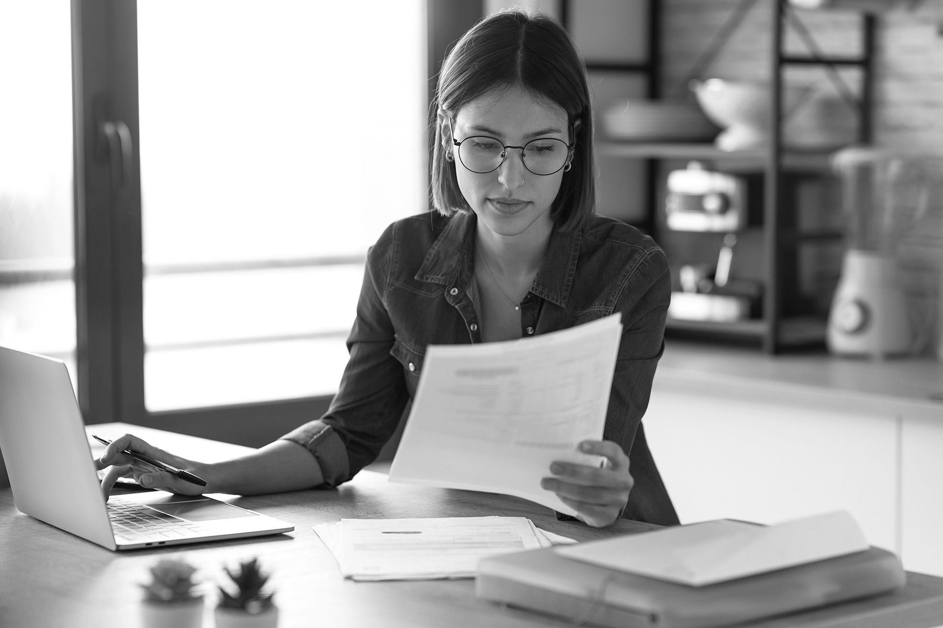 Une personne portant des lunettes est assise à un bureau et travaille sur un ordinateur portable.