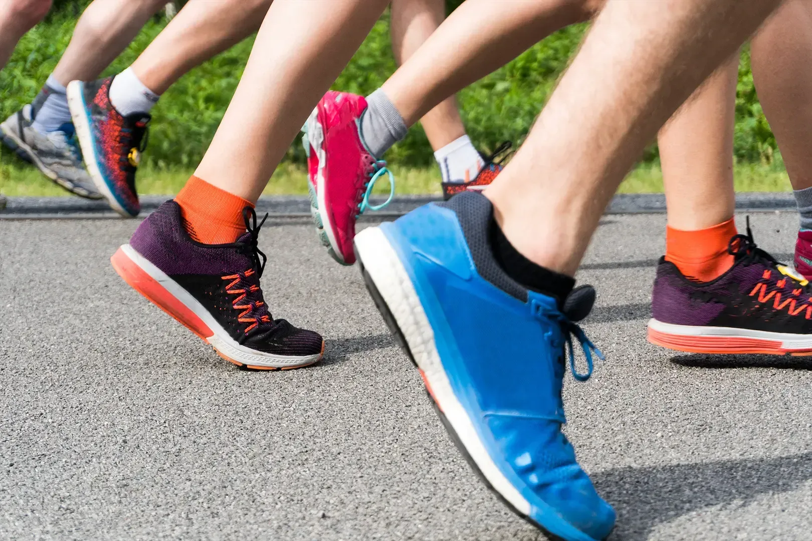 Beine und Füße von Läufern in farbenfrohen Laufschuhen auf einem gepflasterten Weg.
