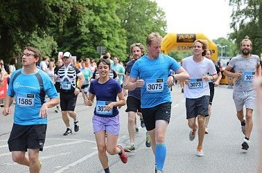Läufer bei einem Wettlauf, einige mit Startnummern, unter einem gelben Bogen.