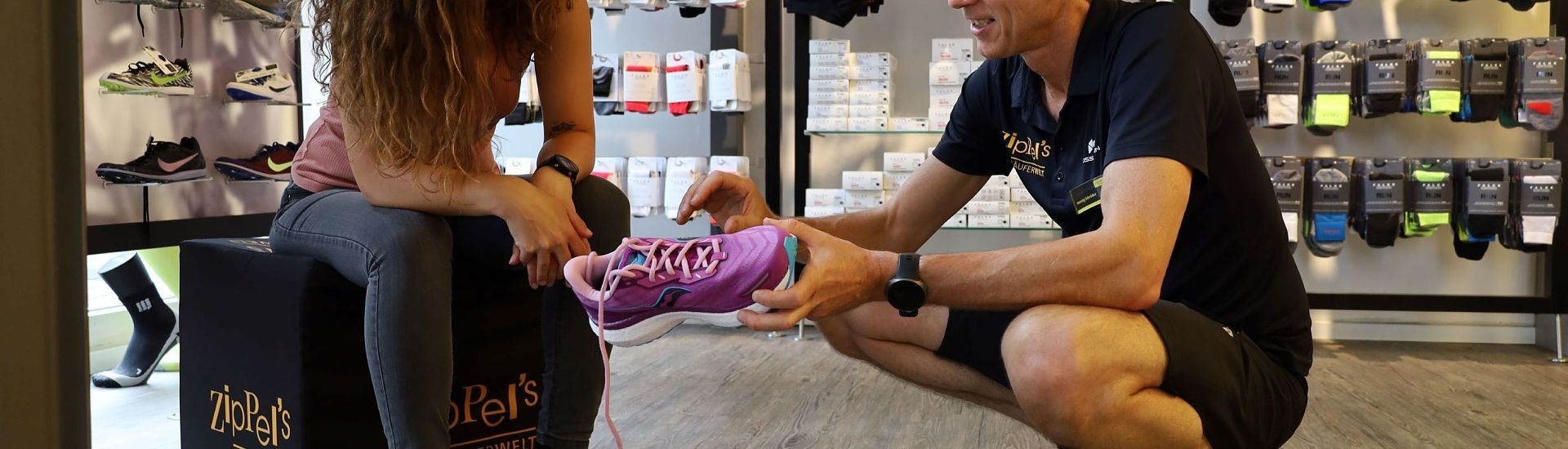 Eine Person in einem Laufschuhgeschäft, der von einem Verkäufer beim Anprobieren eines lila Schuhs geholfen wird.