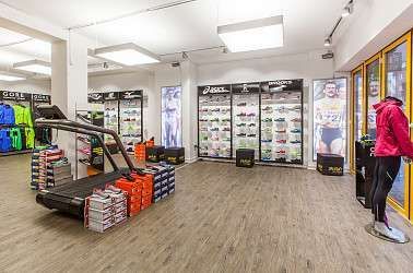 Innenansicht eines Laufschuhgeschäfts mit Laufband, Schuhen und Sportbekleidung in der Auslage.