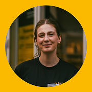 Eine Frau in schwarzem Hemd lächelt in die Kamera, innerhalb eines gelben Kreises.