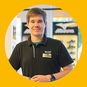 Ein Mann in einem schwarzen Poloshirt steht lächelnd in einem Schuhgeschäft.