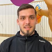 Ein lächelnder Mann mit Spitzbart und schwarzer Kapuzenjacke. Im Hintergrund ist ein Bein mit einem Laufschuh zu sehen.