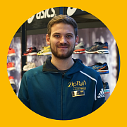 Ein Mann in einer blauen Jacke steht in einem Schuhgeschäft; im Hintergrund sind Schuhe der Marken Asics und Adidas zu sehen.