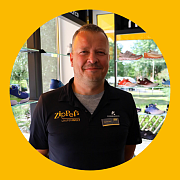 Ein Mann in einem schwarzen Poloshirt steht lächelnd in einem Schuhgeschäft.