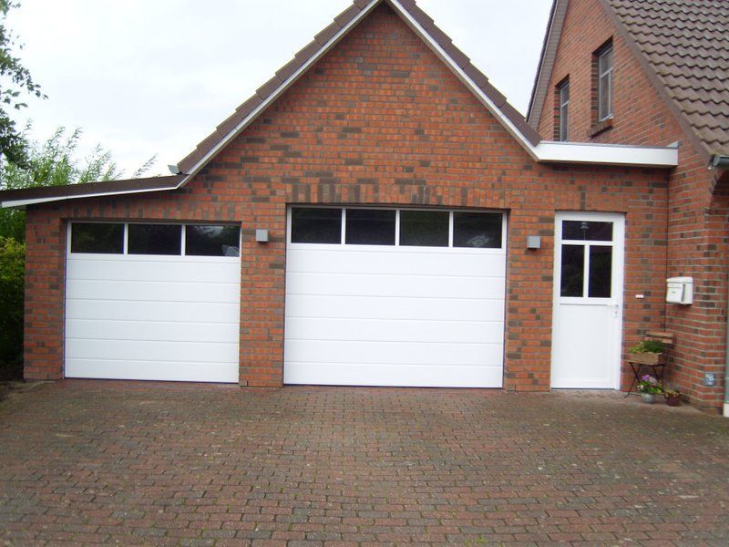 Ein rotes Backsteinhaus mit zwei weißen Garagentoren
