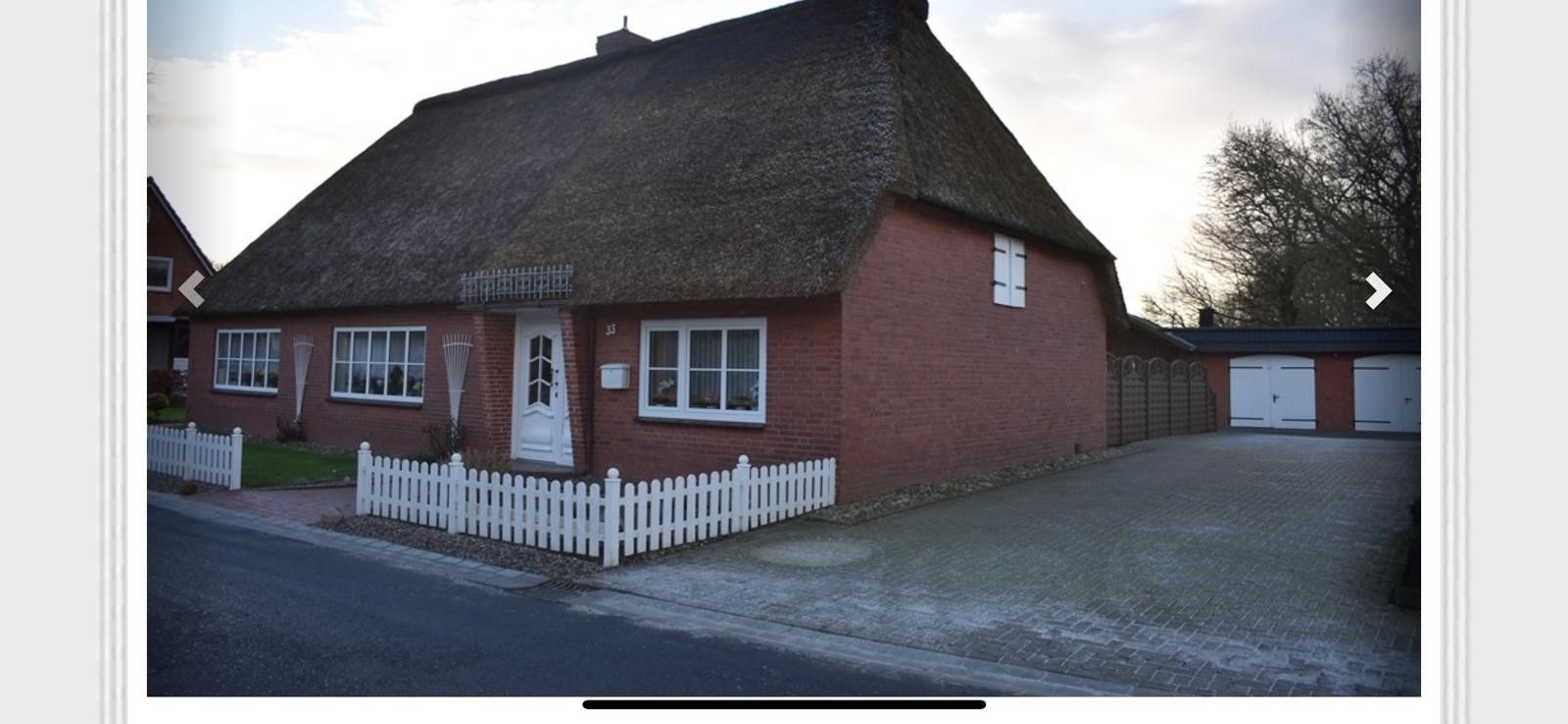 Ein Backsteinhaus mit Strohdach und weißem Zaun