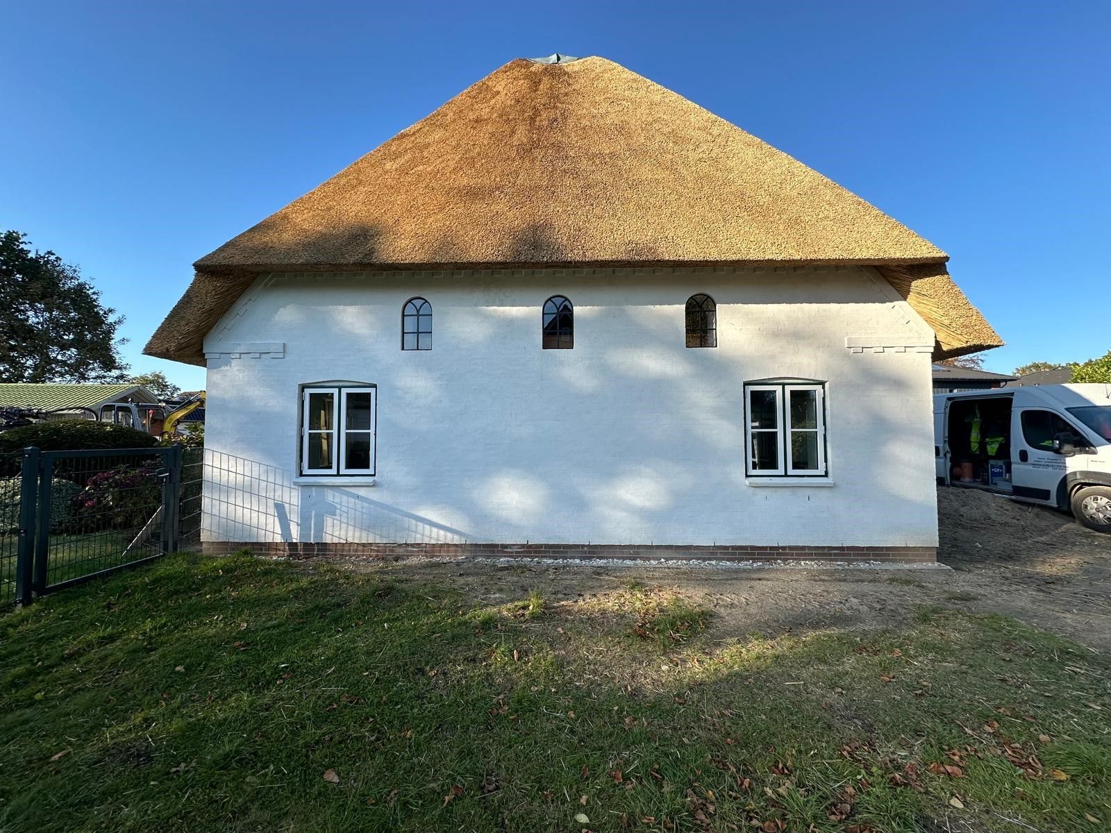 Ein weißes Haus mit Strohdach und ein davor geparkter weißer Lieferwagen.