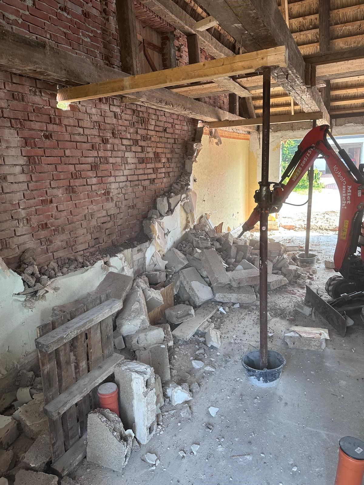 Eine Backsteinmauer wird mit einem roten Bagger abgerissen.