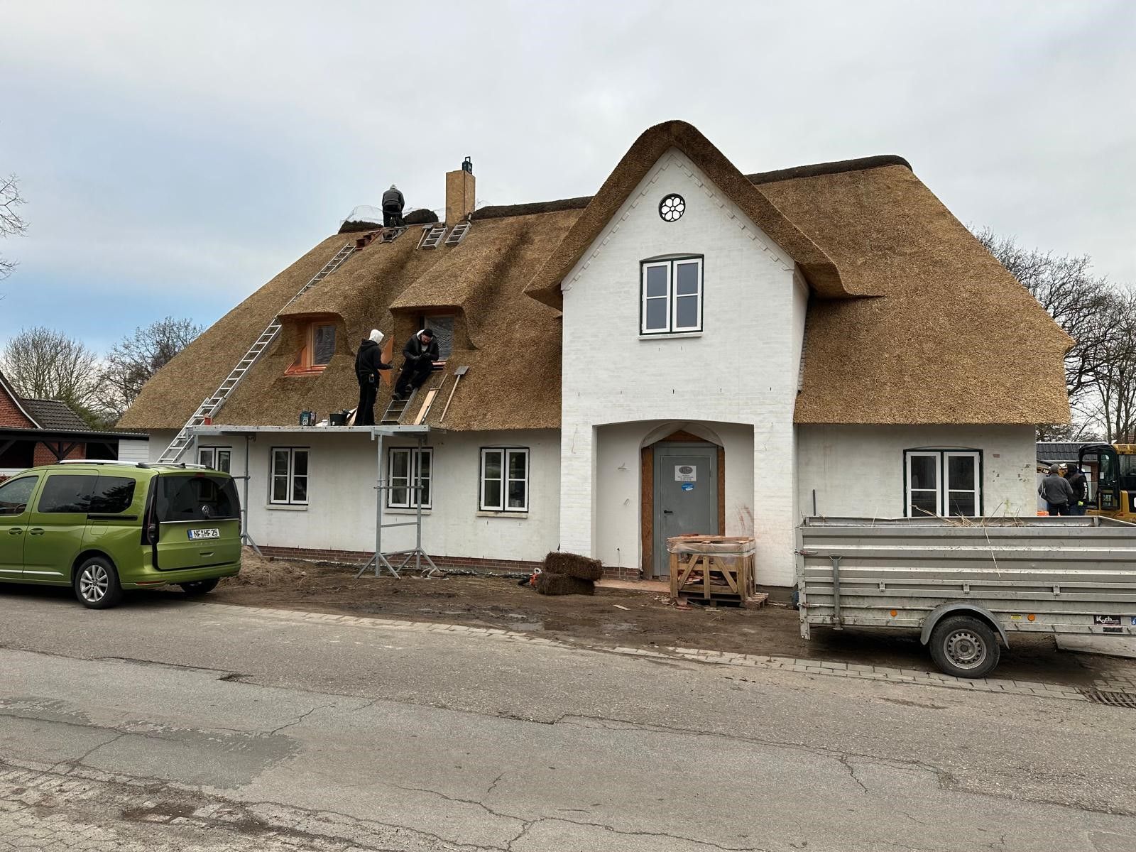 Ein weißes Haus mit Strohdach und ein grüner Lieferwagen davor geparkt.