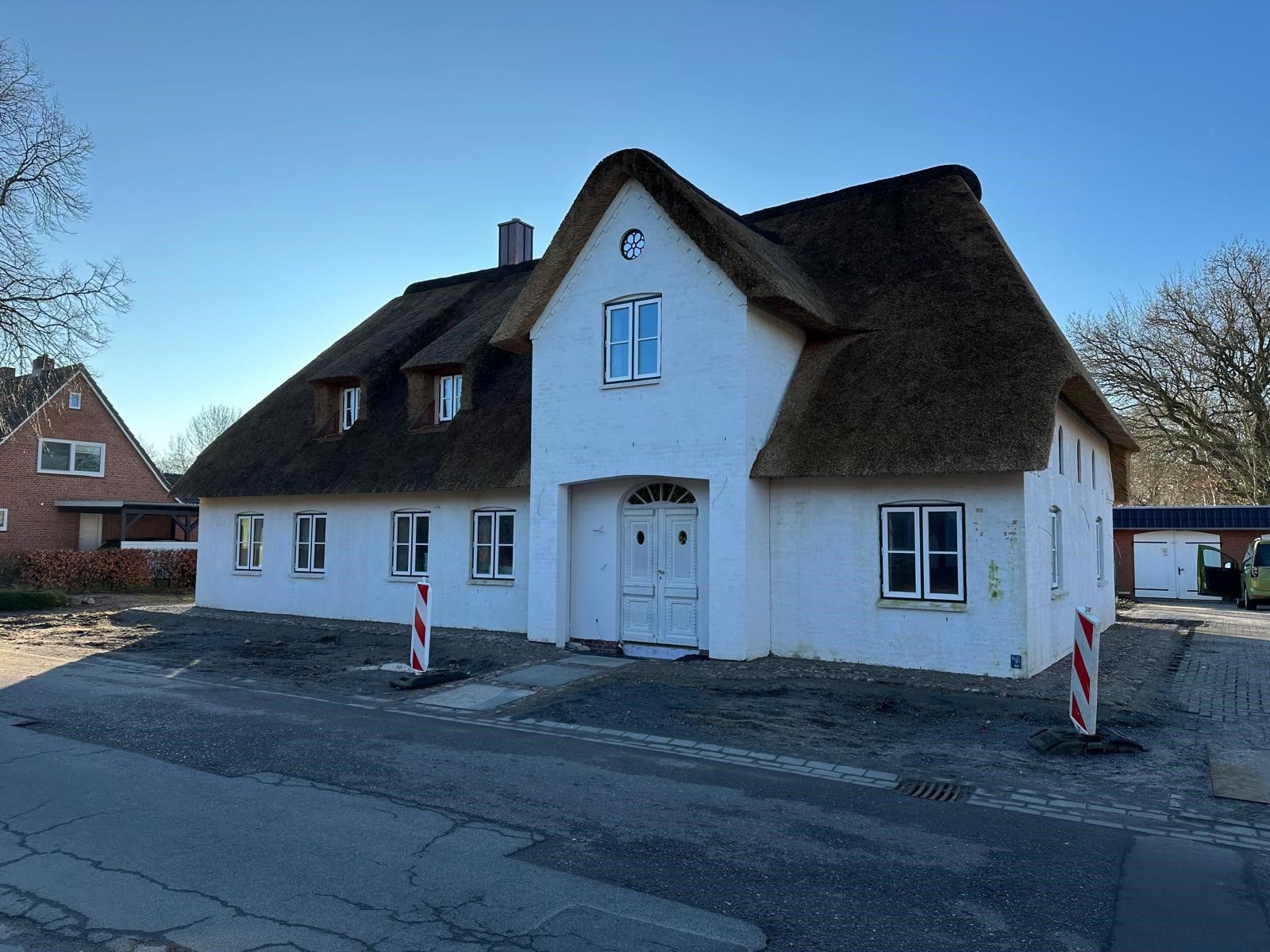 Am Straßenrand steht ein weißes Haus mit Strohdach.