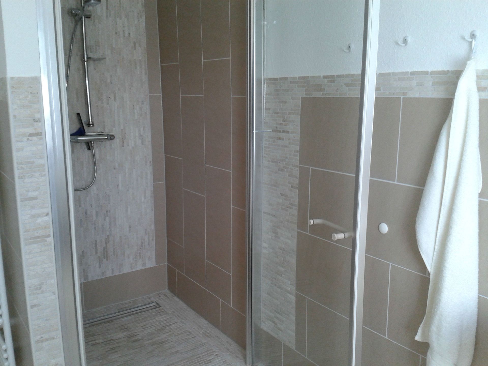 Ein Badezimmer mit ebenerdiger Dusche und einem an der Wand hängenden Handtuch