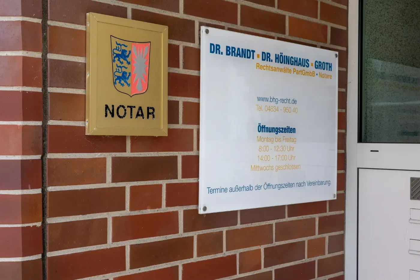 Backsteinmauer mit einem notariell beglaubigten Büroschild und einer hölzernen „NOTAR“-Plakette neben einer Tür
