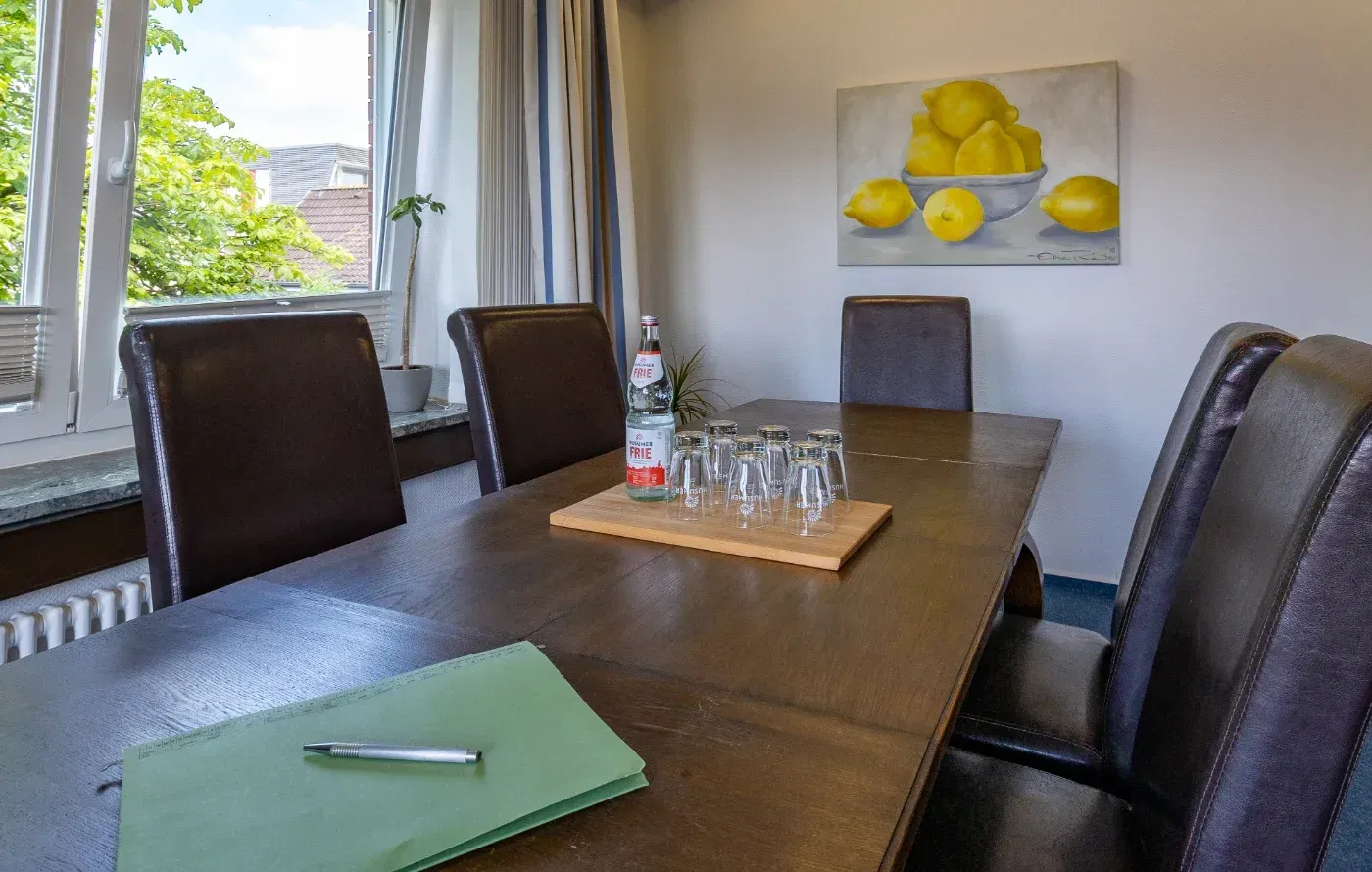 Konferenzraum mit dunklem Tisch, Ledersesseln, Fensterlicht und einer Schale mit Zitronen als Wandbild.