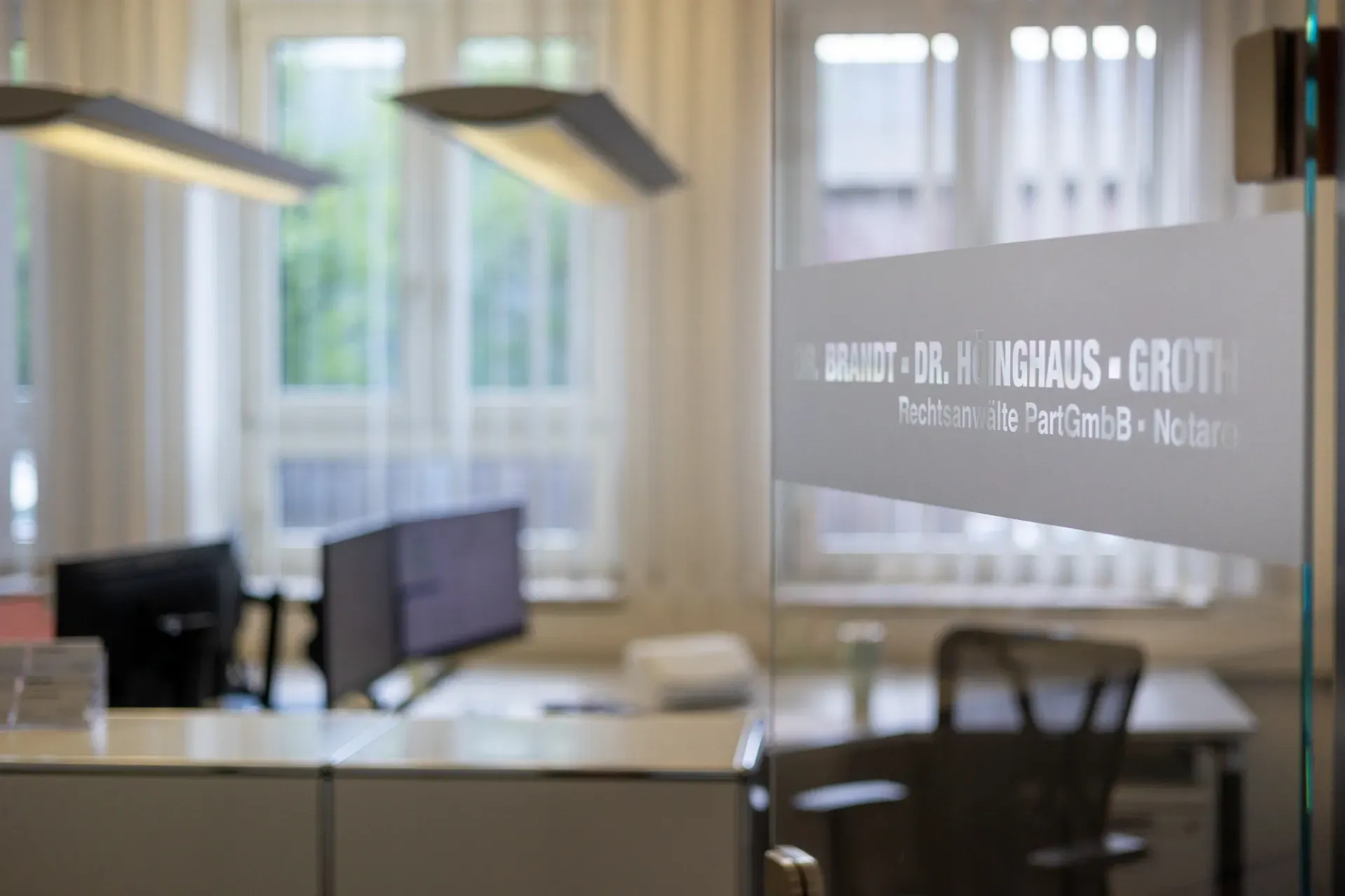 Verschwommenes modernes Büro mit Schreibtischen, Monitoren und Hängelampen hinter einer Milchglastür