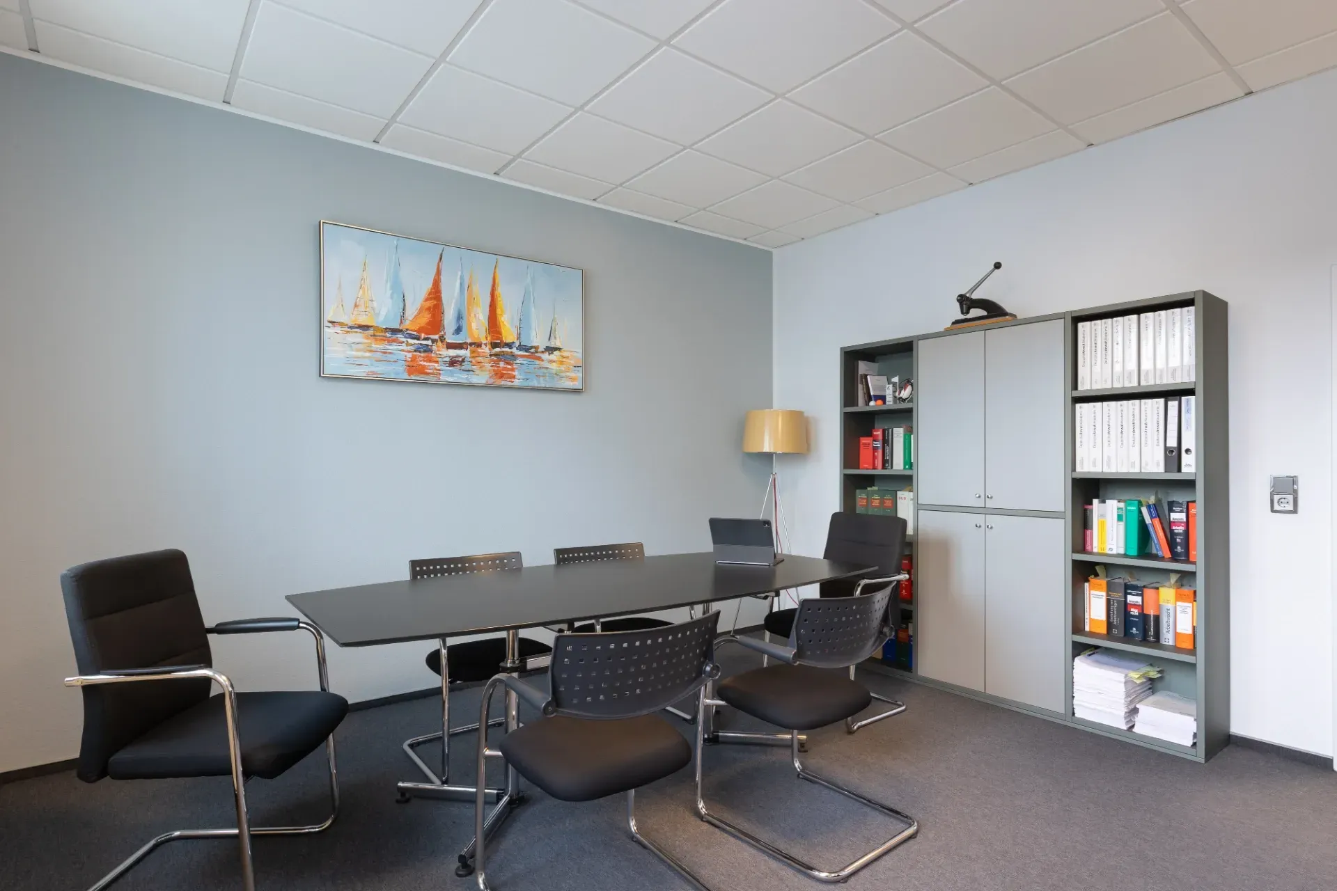 Moderner Konferenzraum mit grauem Tisch, schwarzen Stühlen, Wandbildern und Bücherregalen
