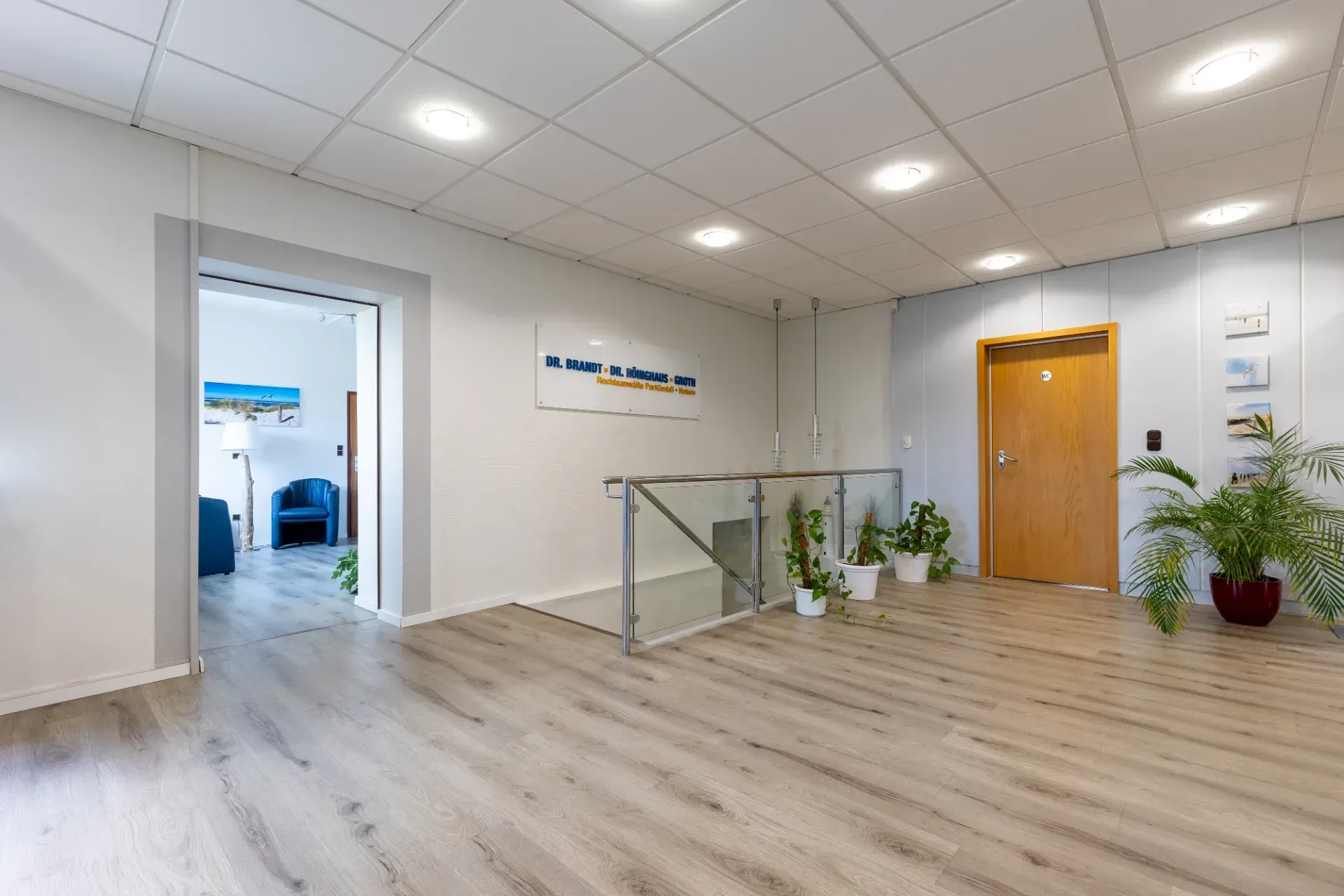 Moderne Bürolobby mit hellem Holzboden, weißen Wänden, Pflanzen, Glasgeländer und Holztür