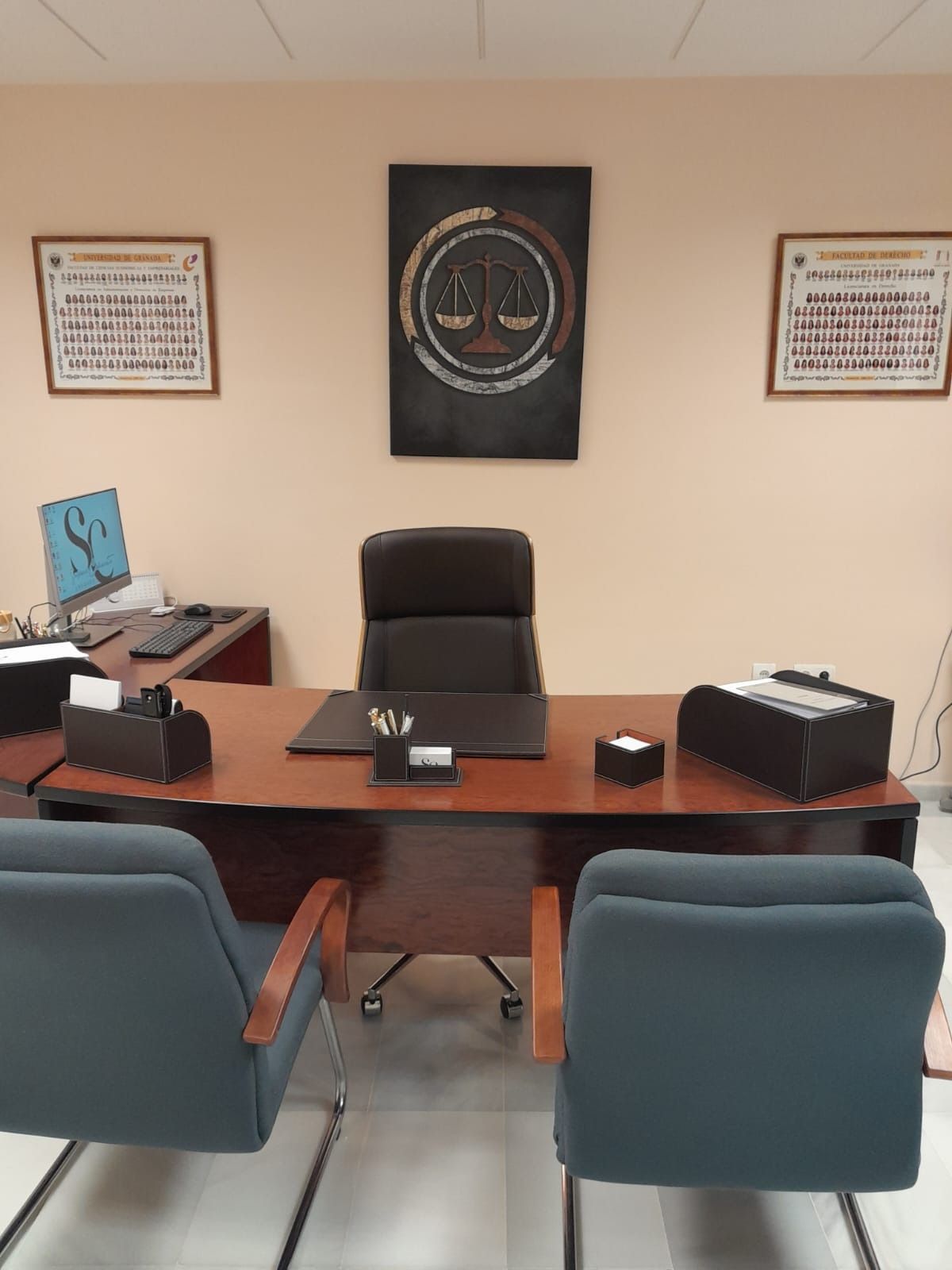 Oficina con escritorio, silla, dos sillas para invitados, cuadros y premios enmarcados en una pared de color beige.