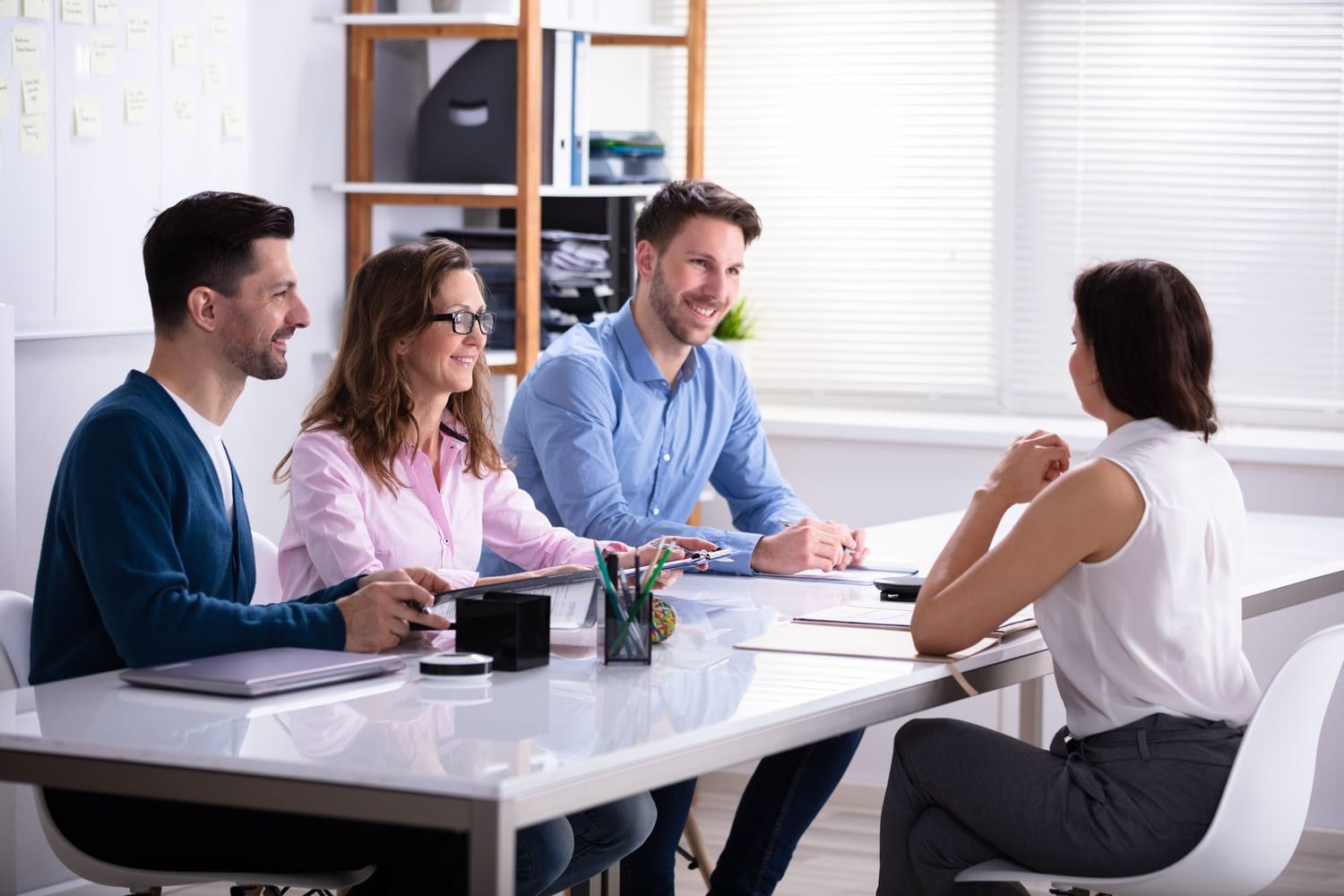 Cuatro compañeros de trabajo en una oficina luminosa, reunidos alrededor de una mesa, charlando y sonriendo.