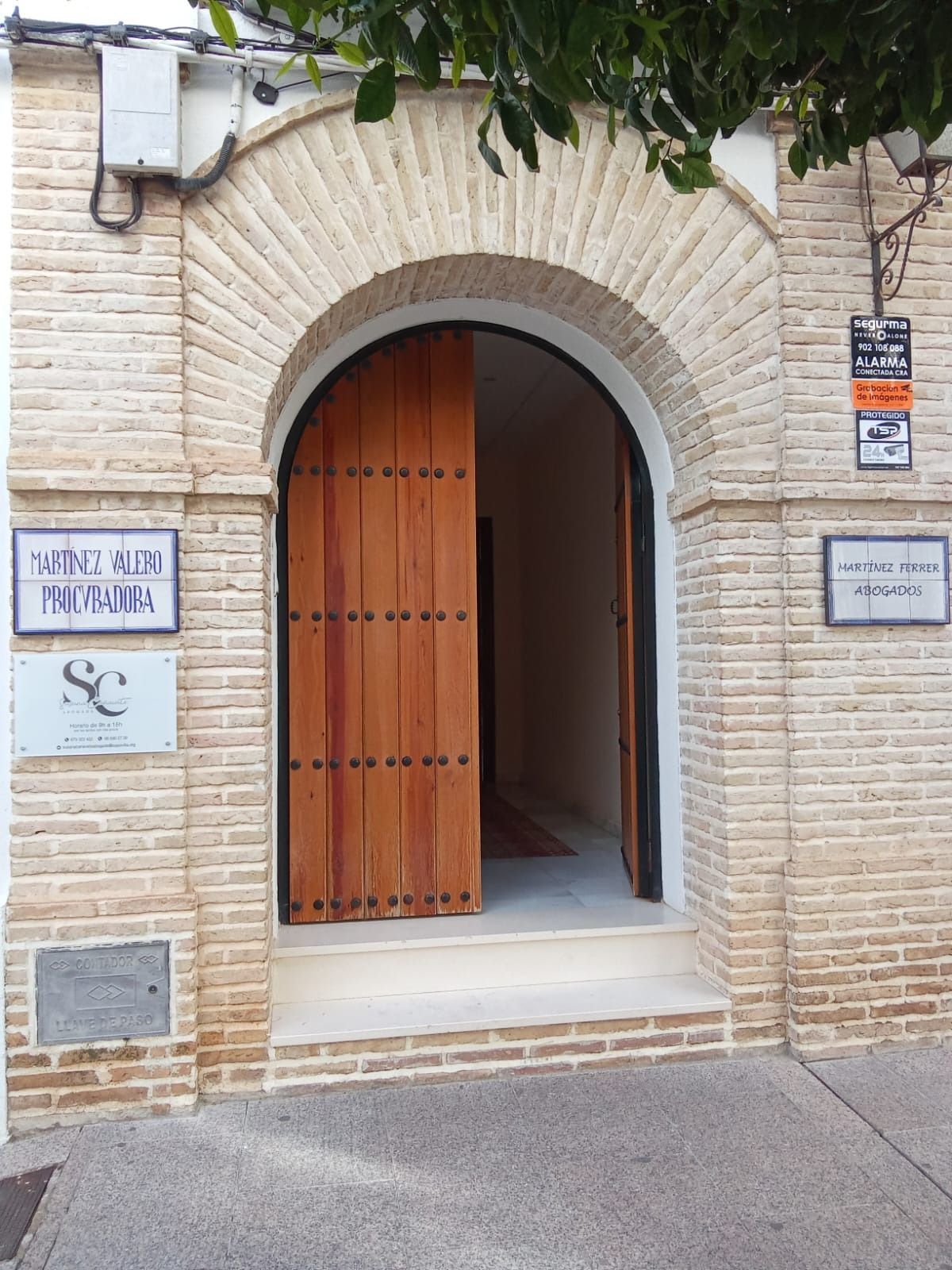 Entrada con arco de piedra, puerta de madera y pequeños letreros en la fachada del edificio.