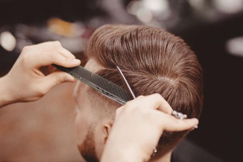 Ein Barbier verwendet Kamm und Effilierschere, um das kurze, gestufte braune Haar einer Person zu stylen. Ein Barbier verwendet Kamm und Effilierschere, um das kurze, gestufte braune Haar einer Person zu stylen.