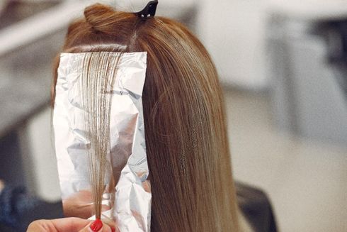 Das braune Haar einer Person wird in einem Salon abgeteilt und mit Farbfolie behandelt. Das braune Haar einer Person wird in einem Salon abgeteilt und mit Farbfolie behandelt.