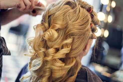 Eine Stylistin verwendet beheizte Lockenwickler, um langes blondes Haar in einem hellen Salonambiente zu stylen. Eine Stylistin verwendet beheizte Lockenwickler, um langes blondes Haar in einem hellen Salonambiente zu stylen.
