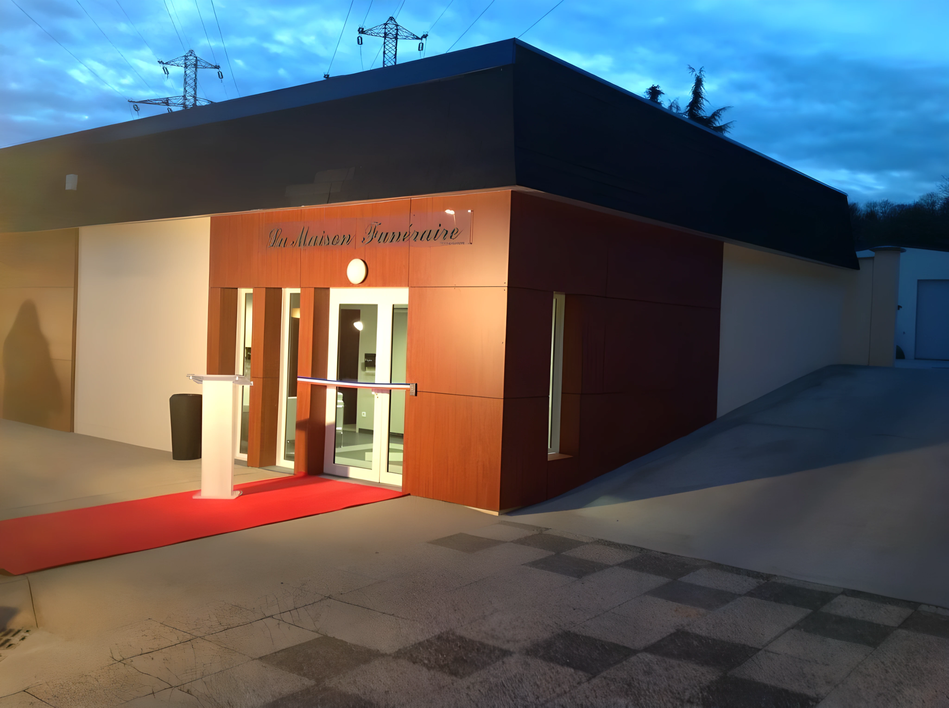 Entrée d'un immeuble moderne au crépuscule, avec tapis rouge et portes vitrées illuminées