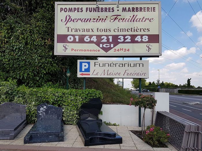 Monument funéraire extérieur avec pierres tombales et grand panneau d'information funéraire en français en bord de route